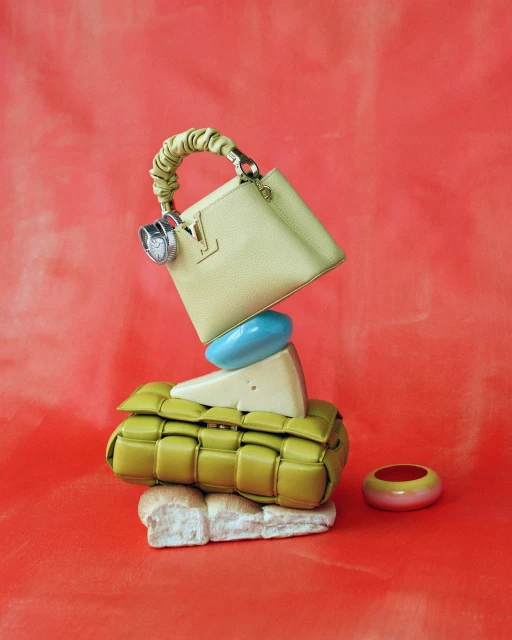 Fashion still life against a red backdrop featuring a purse, jewelry, wedge of cheese, bread and a purse in a stacked arrangement.