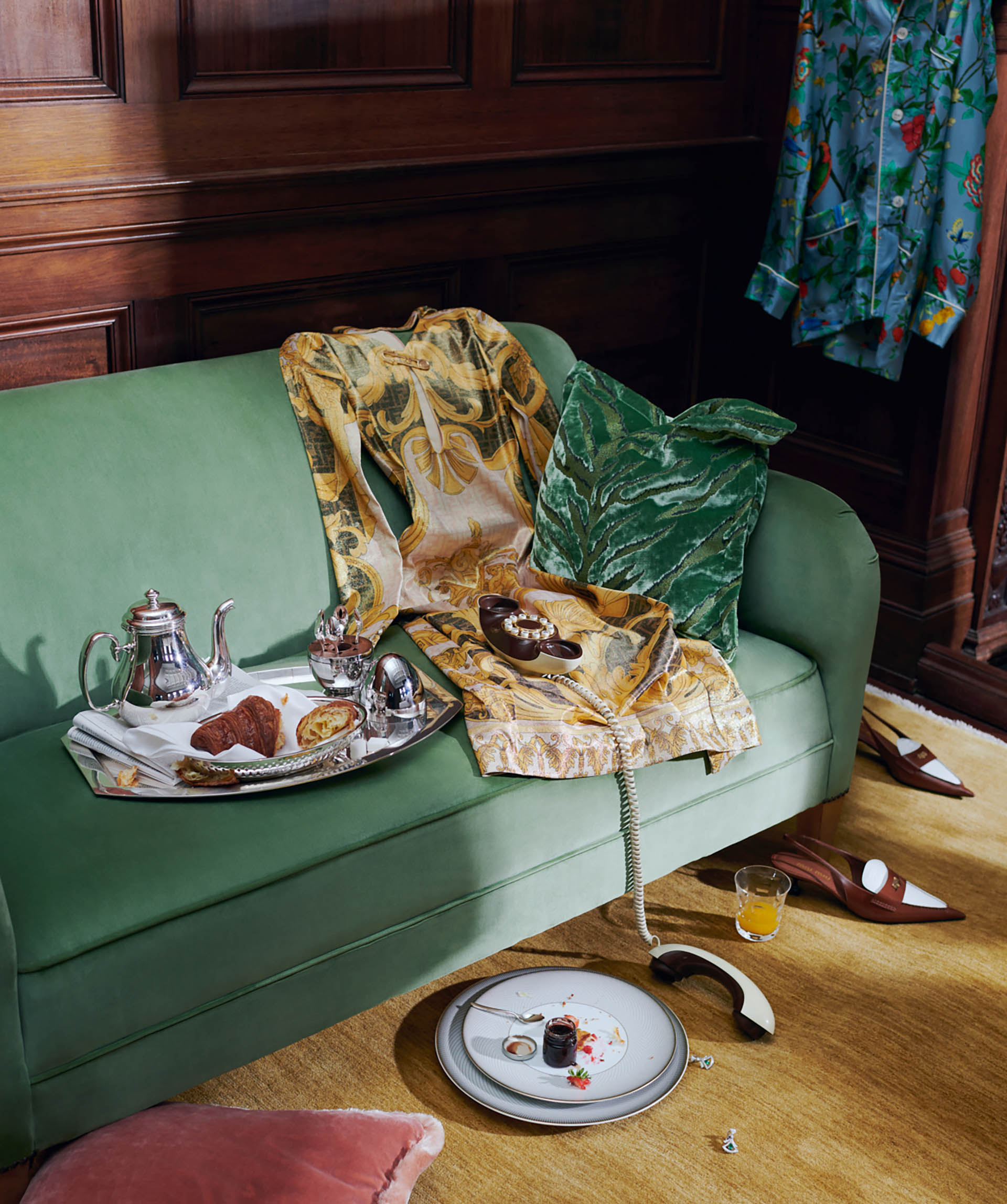 Still life photograph featuring breakfast set on a green couch, including a pastry, silverware, dishes, orange juice, and clothing.