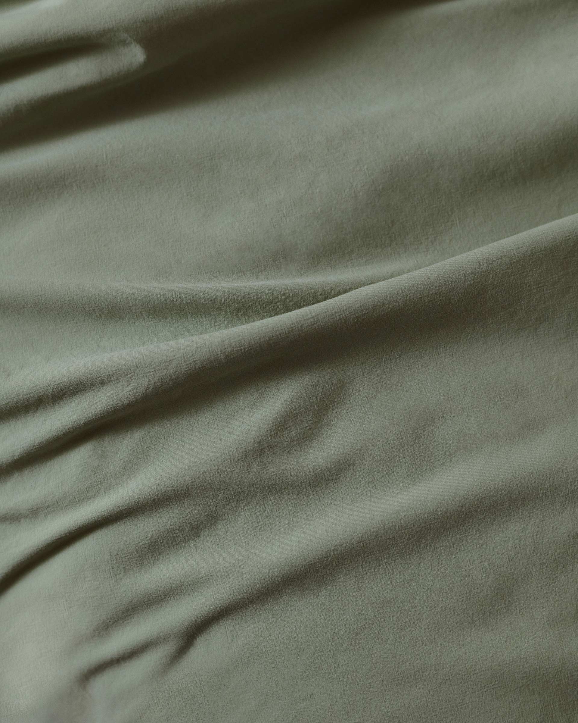 Close-up of sage green textile fabric with soft, diffused lighting emphasizing its draped folds and subtle texture.