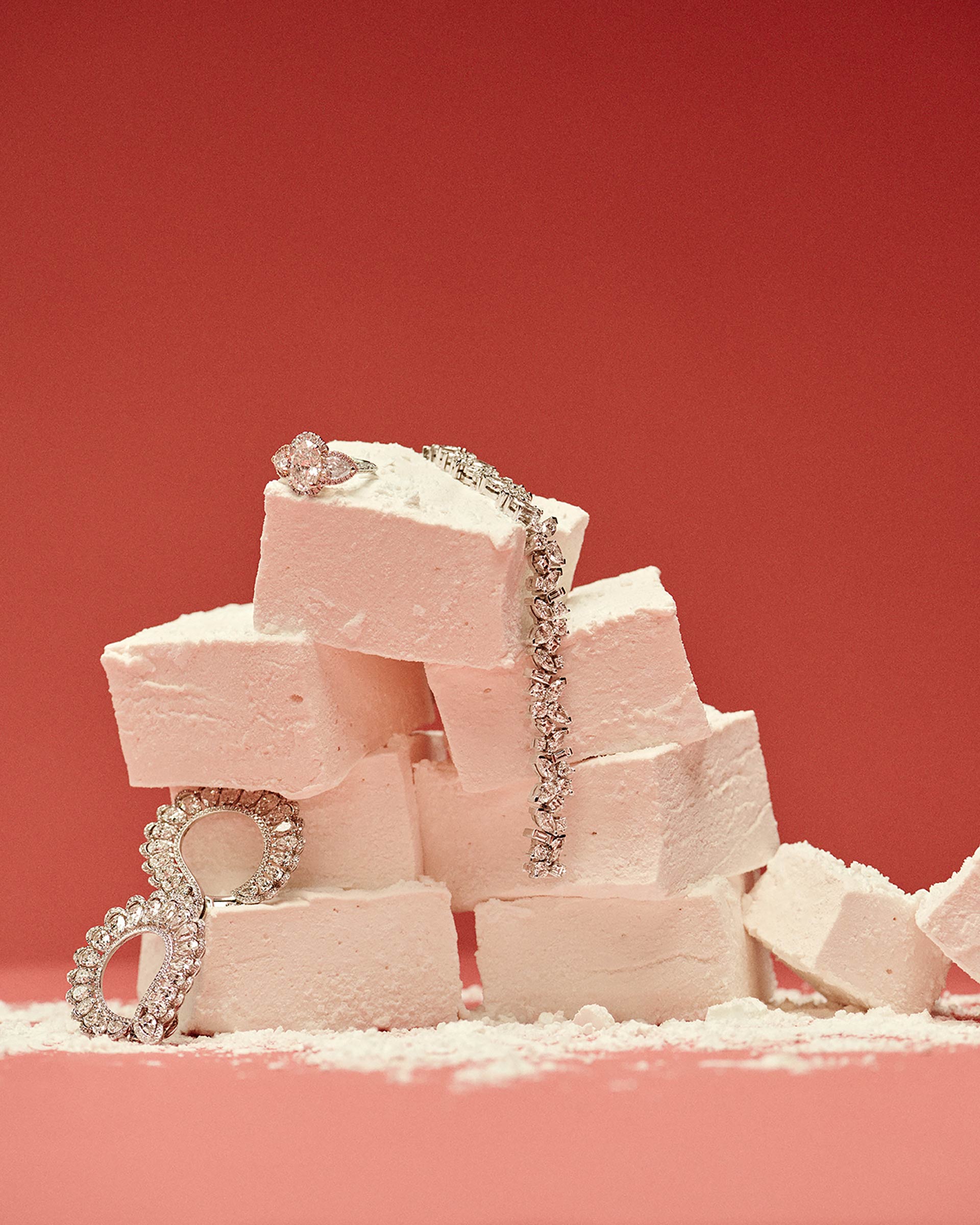Jewelry on a stack of white marshmallows against a red backdrop. A diamond ring and bracelet catch the eye.