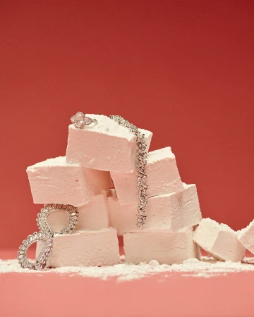 Jewelry on a stack of white marshmallows against a red backdrop. A diamond ring and bracelet catch the eye.