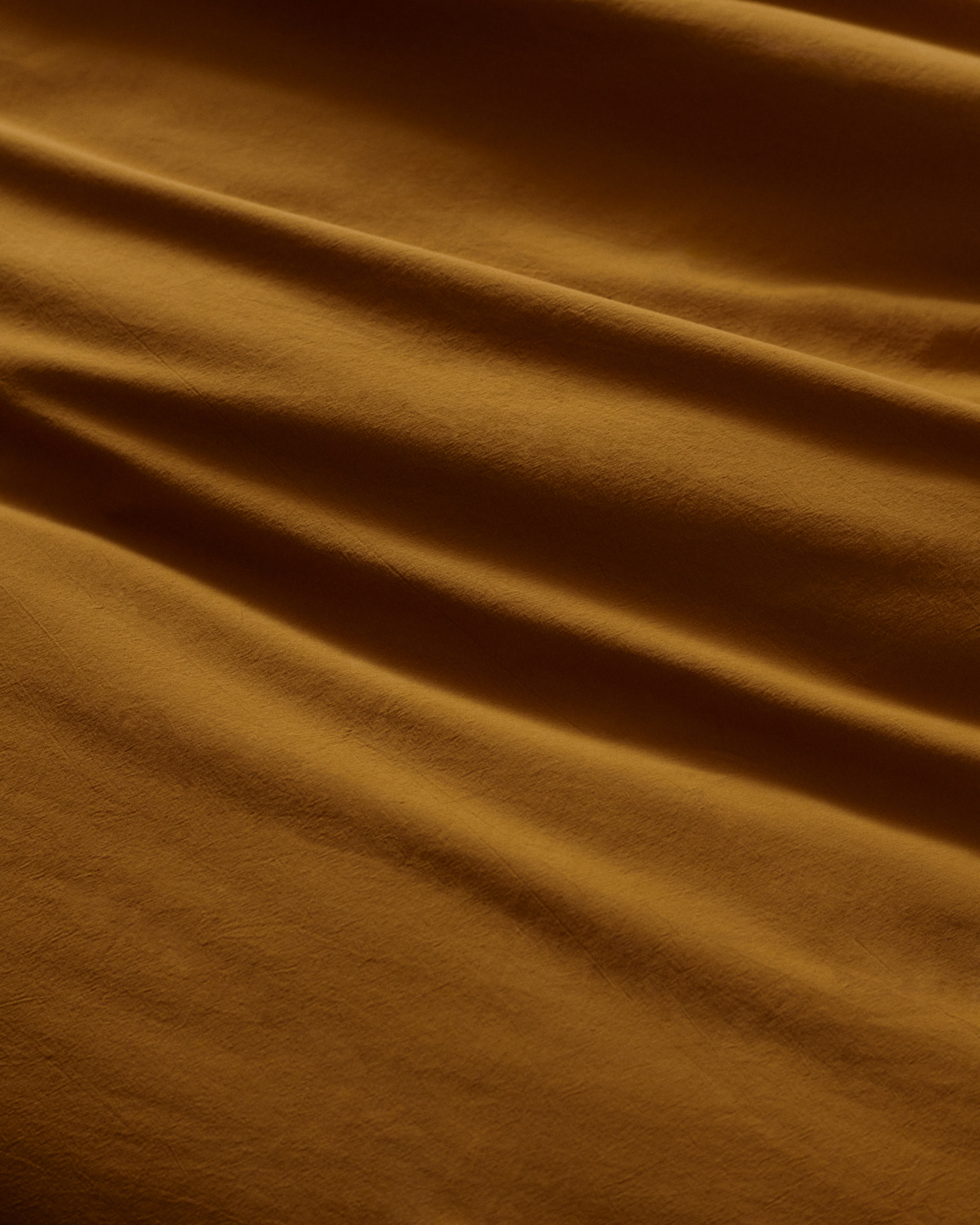 Abstract shot of golden tan textile fabric with soft, smooth folds, creating a warm, inviting textured background or backdrop.