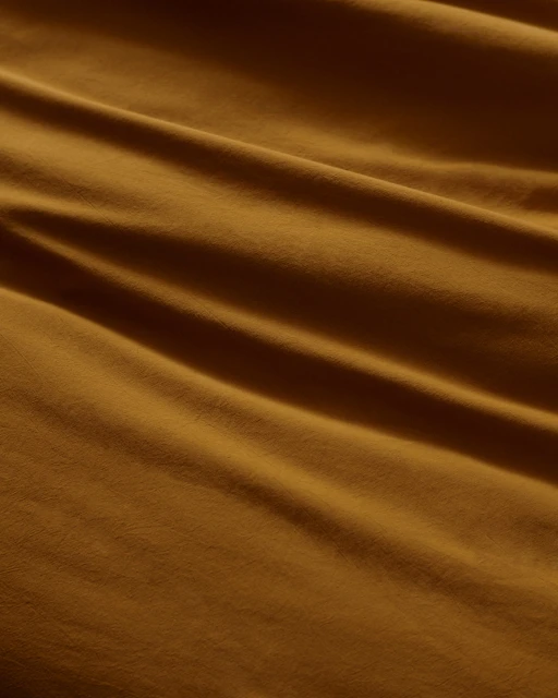 Abstract shot of golden tan textile fabric with soft, smooth folds, creating a warm, inviting textured background or backdrop.