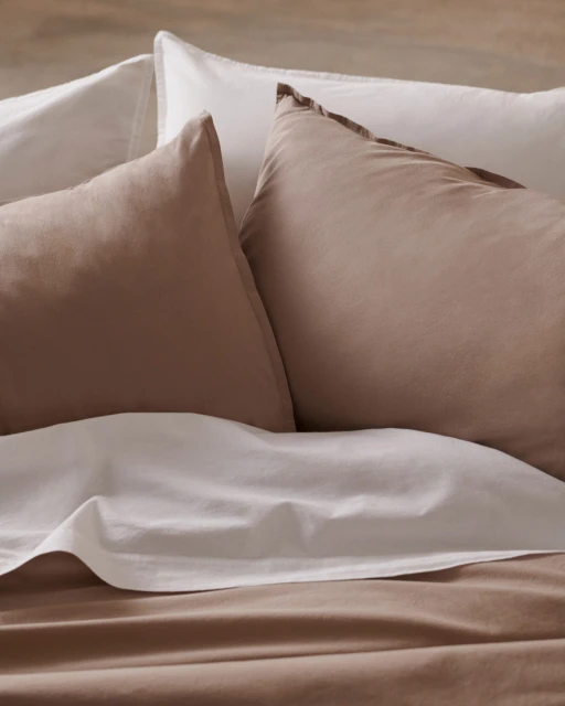 Close-up of a bed featuring soft, tan and white linens and pillows, offering a textured and comfortable sleep environment.