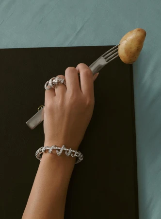 Close-up of a hand wearing diamond rings and bracelet holding a fork with a potato