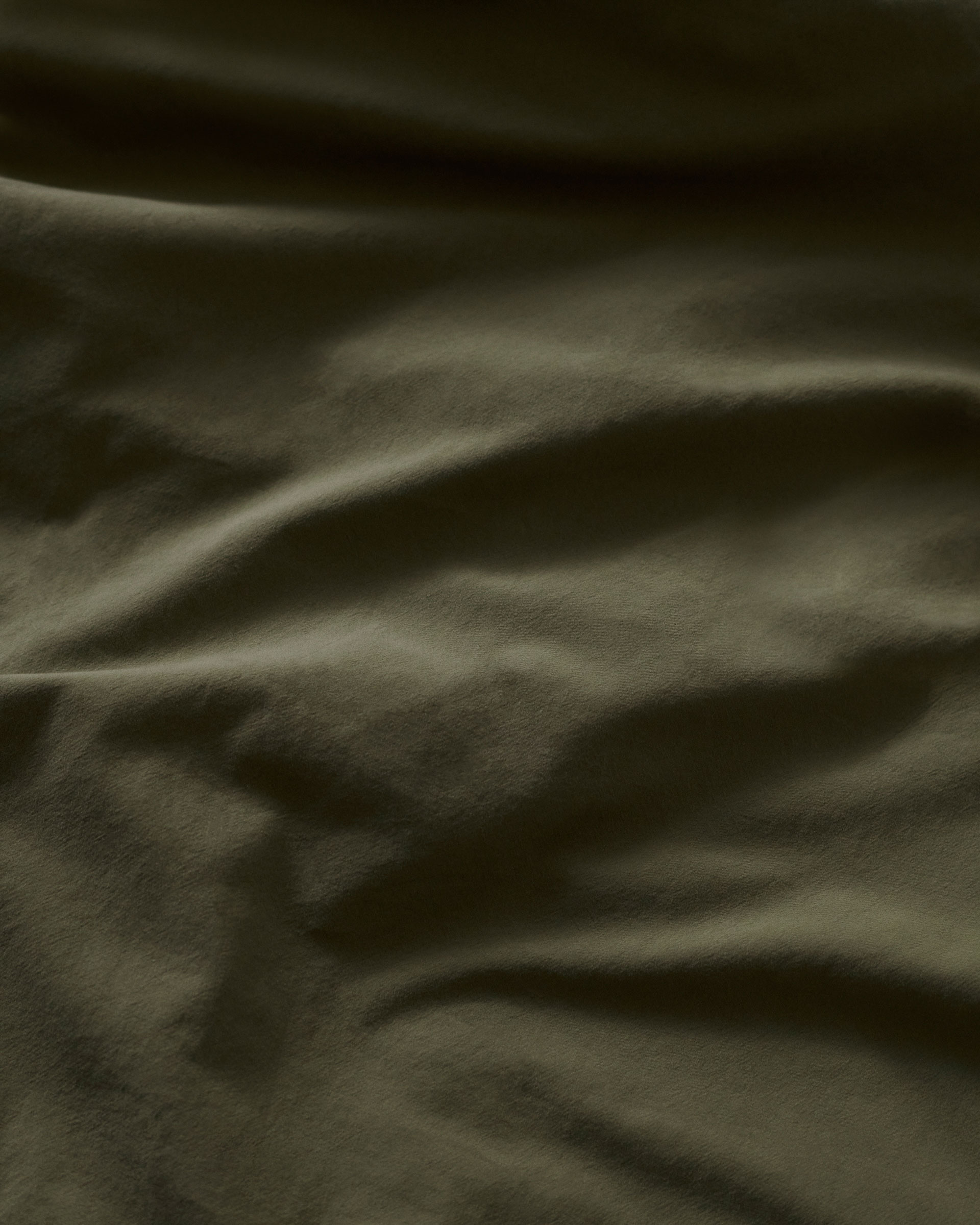 Close-up of wrinkled green fabric with a subtle sheen, showing depth and texture, ideal for backgrounds or material studies.
