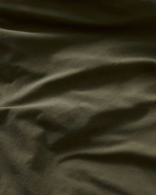 Close-up of wrinkled green fabric with a subtle sheen, showing depth and texture, ideal for backgrounds or material studies.