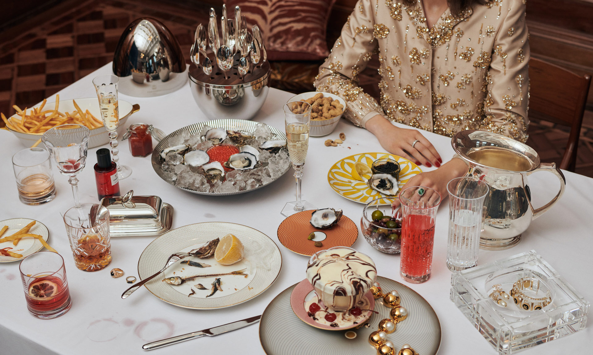 Opulent table setting with oysters, caviar, dessert, French fries, champagne, and cocktails arranged for an indulgent culinary experience.