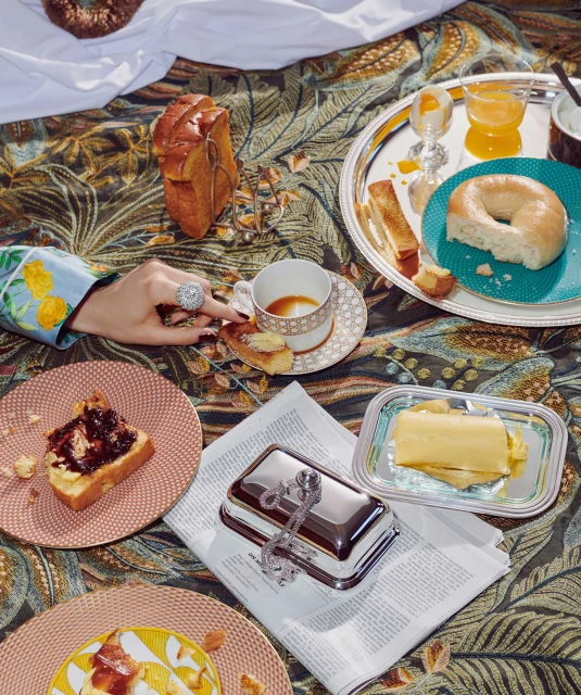 Overhead shot of an indoor brunch with toast, bread, pastries, coffee, butter, and orange juice arranged on patterned textile.