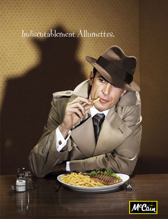 Retro-style advertising photo of a man in a tan trench coat and fedora at a table eating french fries, with a dark shadow behind him.