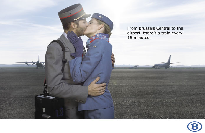 Airport embrace: Flight attendant and man in uniform share a kiss on the runway with planes in the background in an advertisement.