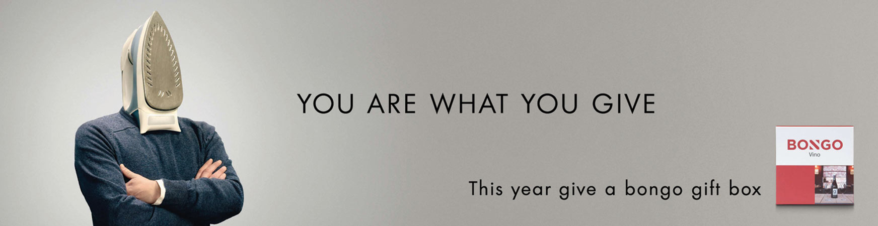 Conceptual advertisement featuring a person with an iron for a head, next to a wine gift box, on a grey background with bold sans-serif text.