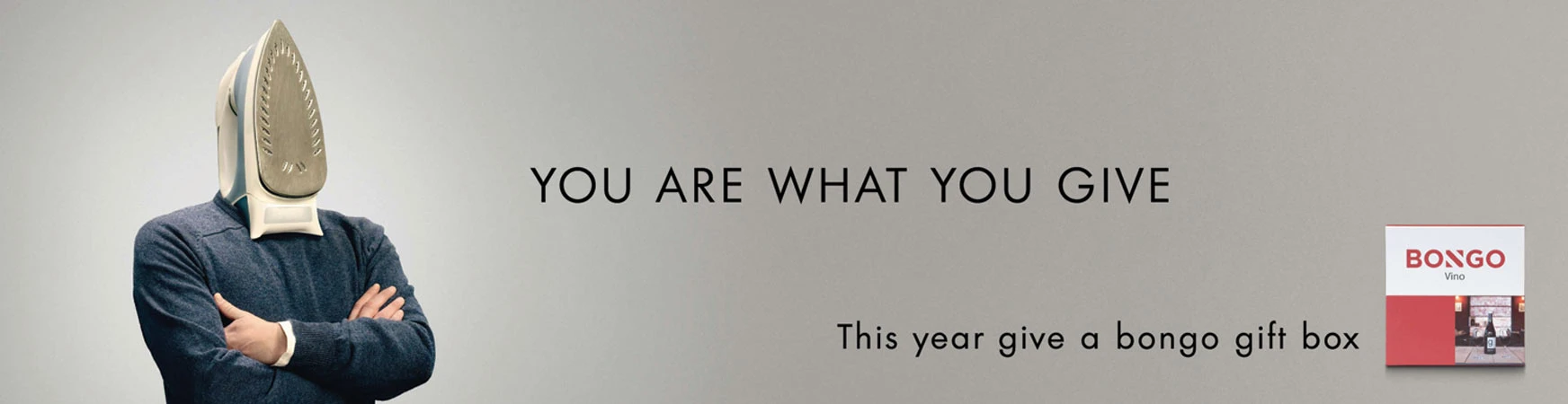 Conceptual advertisement featuring a person with an iron for a head, next to a wine gift box, on a grey background with bold sans-serif text.