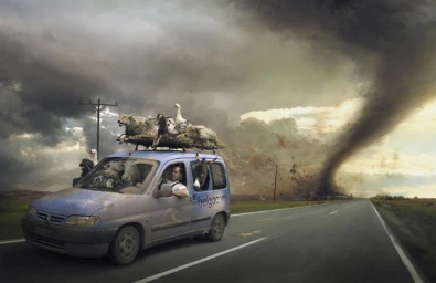 Blue van driving on an open road with farm animals inside and on top as a massive tornado approaches in the background.