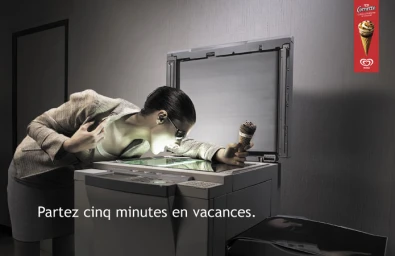 Woman leaning over an open office photocopier holding an ice cream cone inside the glowing glass plate in a dimly lit room.