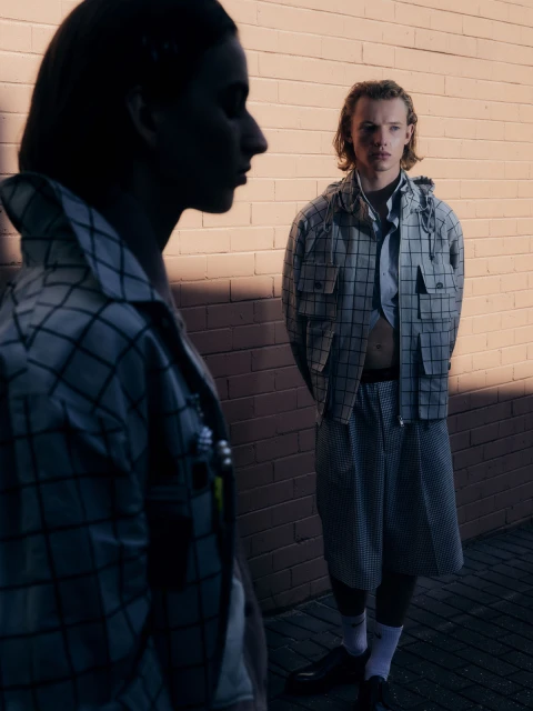 Two fashion models wearing matching checkered outfits standing against a brick wall, demonstrating contemporary style and urban fashion.