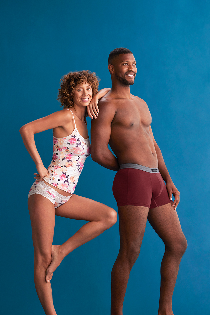 Studio shot of an attractive smiling mixed ethnicity couple in underwear posing against a solid blue backdrop. Fashion and beauty concept.
