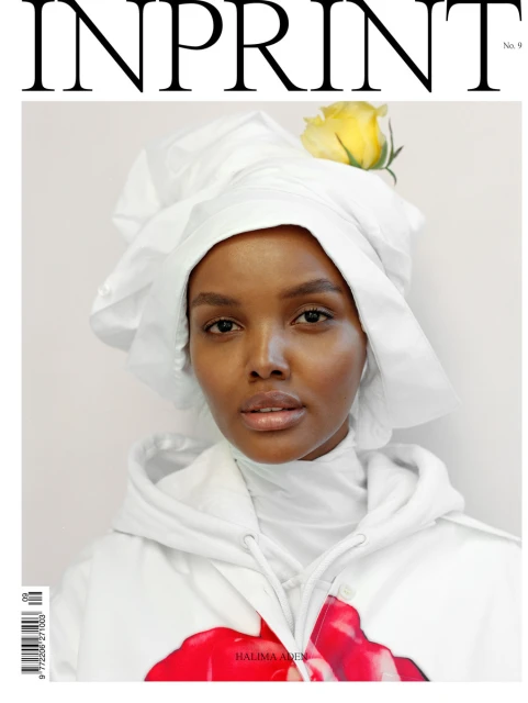 Magazine cover featuring Halima Aden in a white hooded top and head covering adorned with a yellow rose, set against a light background.