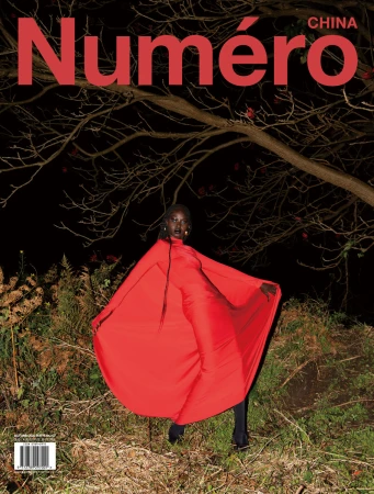 Black woman in a vibrant red dress with a draped cape posing outdoors at night under a tree.