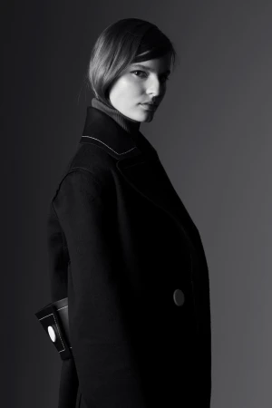 Model in a dark coat with contrasting white stitching styled by Michelle Jank against a grey background.