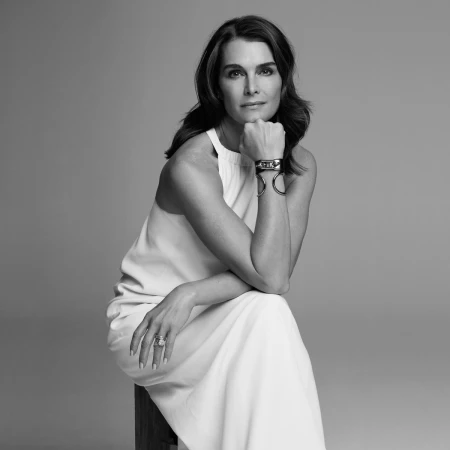 Monochrome portrait of Brooke Shields seated wearing a white halter-neck dress and chunky metal cuff bracelet.