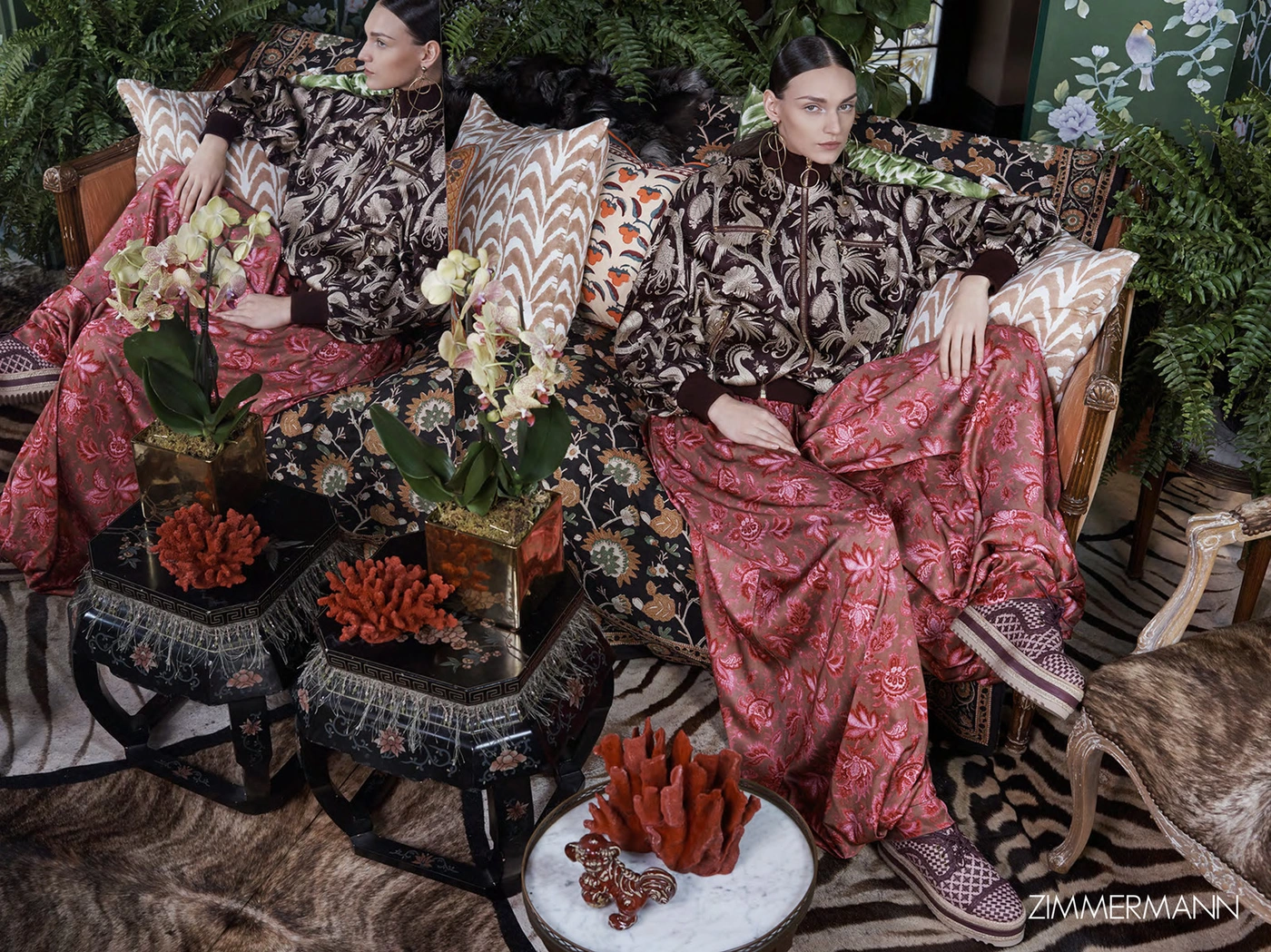 Woman in patterned brown jacket and floral skirt seated on an ornate sofa with orchids and coral decor styled by Michelle Jank