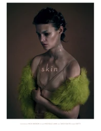 A woman wearing a nude bra and a fluffy lime green fur wrap, styled with hair pins, against a dark studio background.