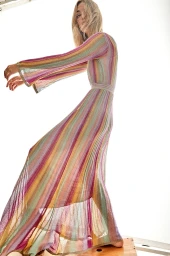 Model wearing a floor-length multicolored striped knit dress posed against a bright white background