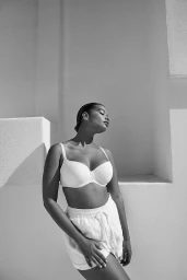 Black and white portrait of a woman wearing a white bra and shorts posing against a light architectural background.