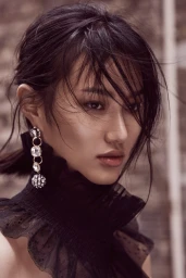 Close-up portrait of a woman with dark hair styling by Budi Juspandi wearing a black ruffled collar and crystal earrings.