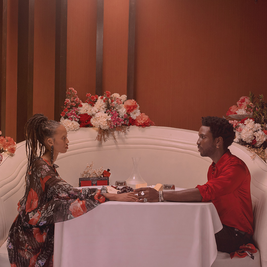 A stylish couple in an indoor setting sits at a table adorned with flowers, creating a romantic atmosphere for their date.