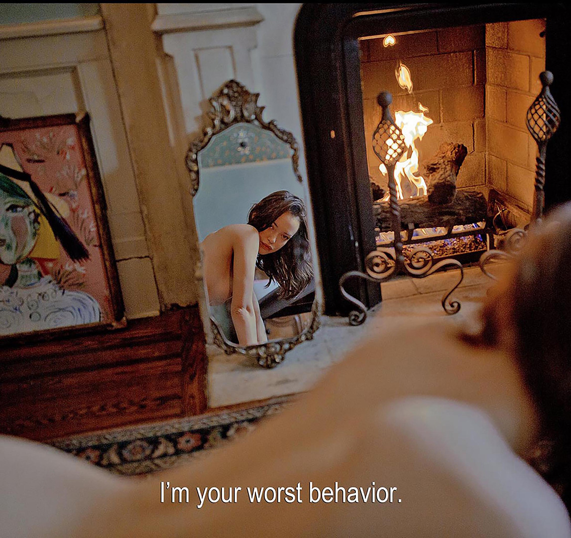Indoor portrait of a brunette woman reflected in a mirror with a fireplace in the background, and text overlay at the bottom.