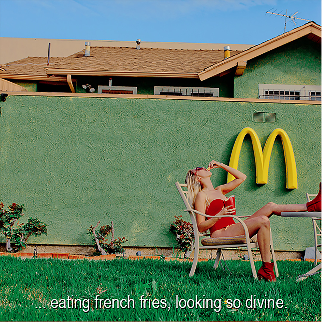 Woman in red swimsuit sits in chair, eating french fries with a McDonald's sign in the background and a green house wall.