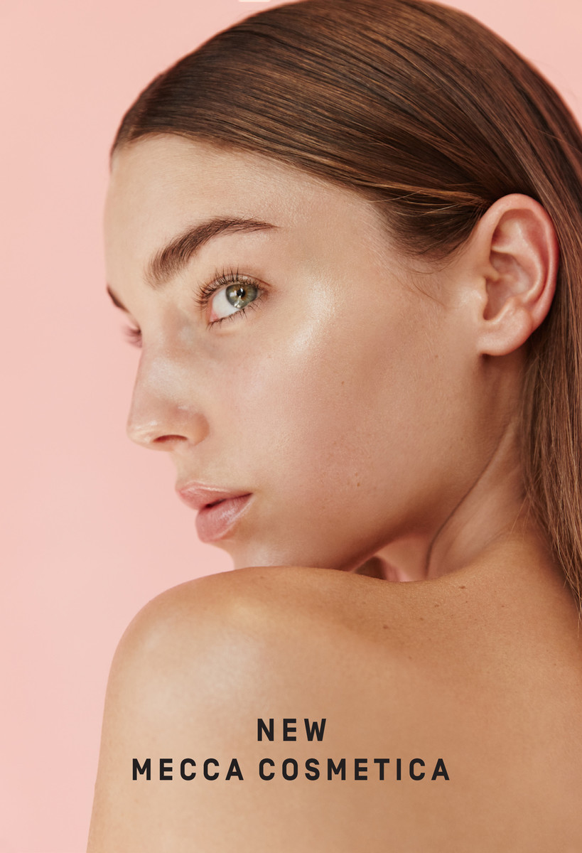 Close-up portrait of a fair-skinned woman with brown hair in a beauty advertisement for Mecca Cosmetica against a peach background.