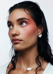 Portrait of a woman with wet dark hair, pink eyeshadow, and diamond butterfly earrings against a white background