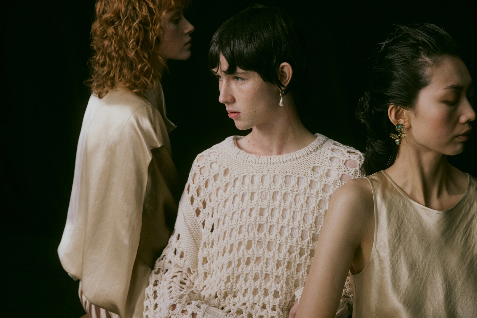 Three models with distinct poses against a dark background in an editorial fashion photograph by Lilli Waters.