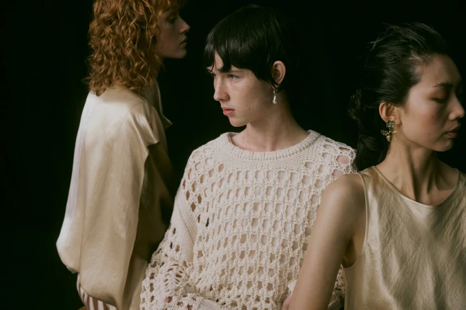 Three models with distinct poses against a dark background in an editorial fashion photograph by Lilli Waters.