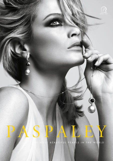 Blonde woman with pearl jewellery. Close-up beauty shot in black and white, she holds a pearl necklace and wears pearl earrings.