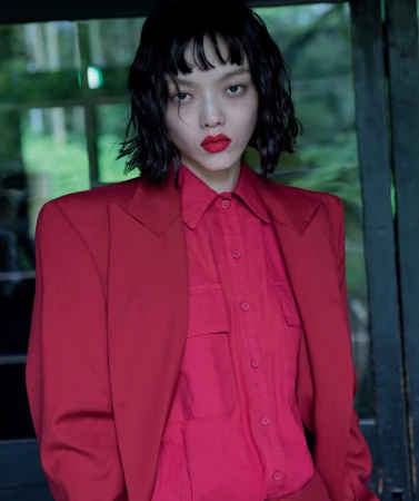 Woman with dark hair and bright red lipstick wearing a red button-down shirt and structured blazer outdoors.