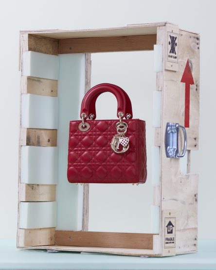 Elevated view of a red Lady Dior handbag with quilted design and silver hardware, displayed in a deconstructed wooden shipping crate.