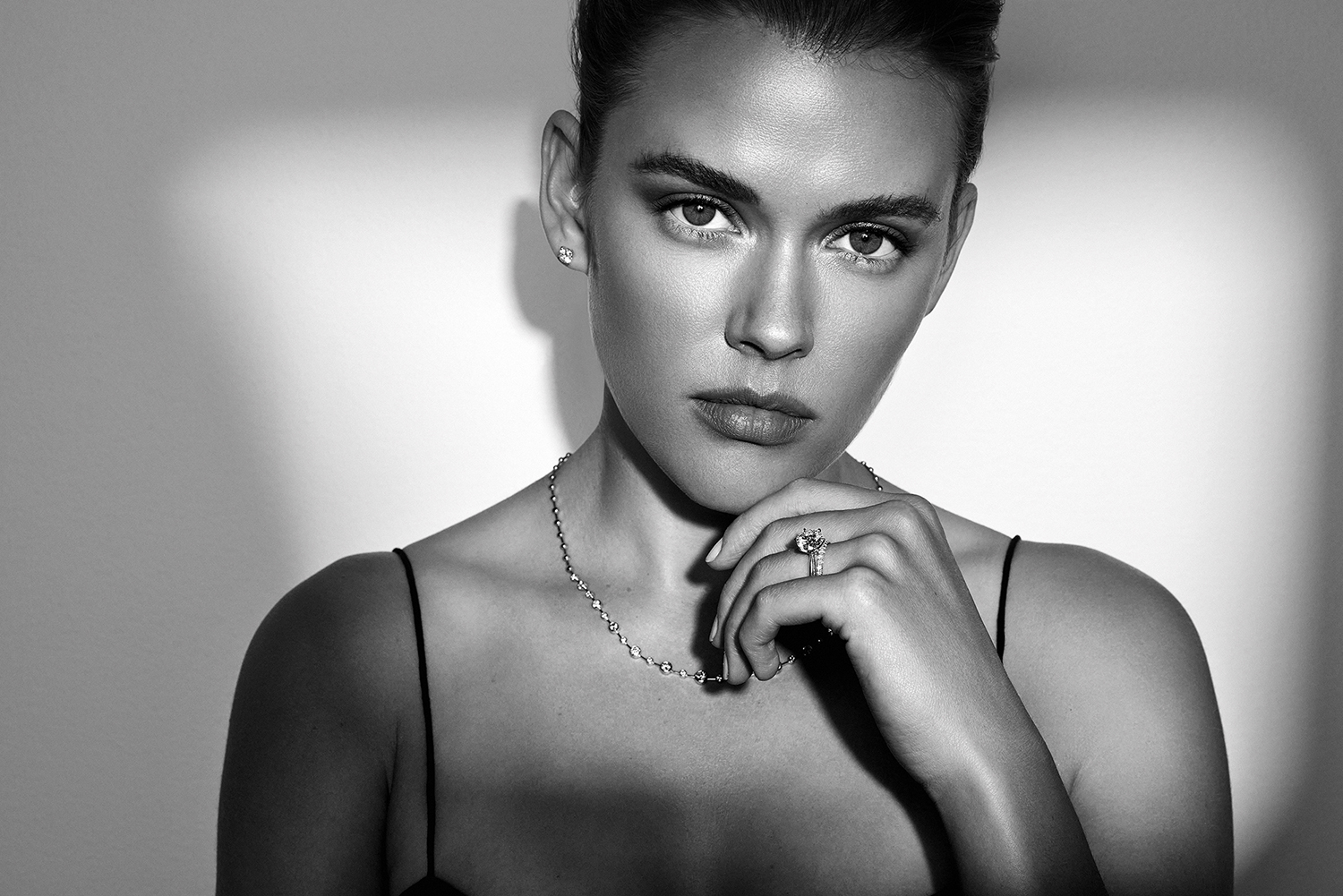Monochrome portrait of a woman with dark hair and light skin, wearing jewelry, posing in a photo studio with soft lighting.
