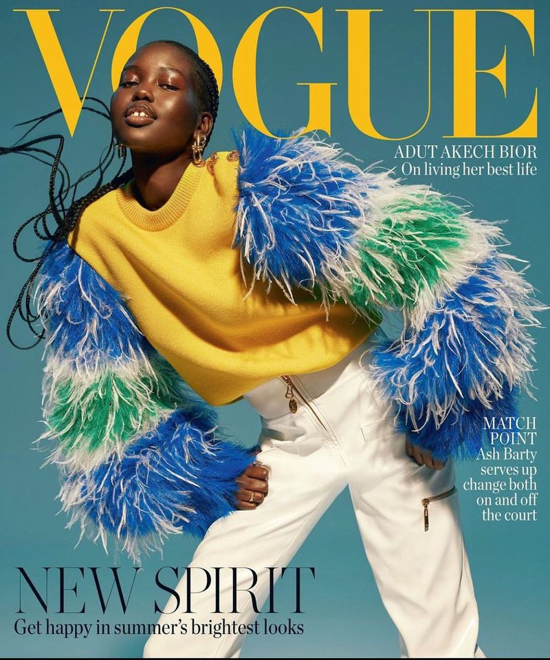 Vogue cover featuring a Black female model in a yellow sweater and colorful feather jacket, posing against a light blue background.