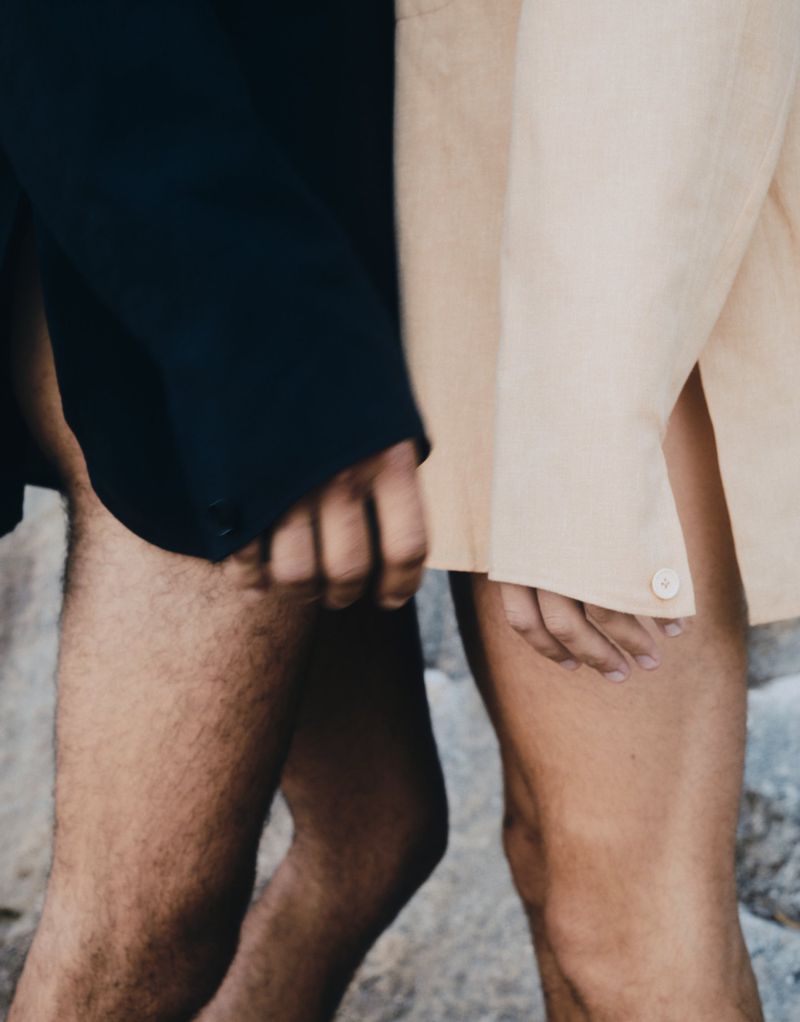 A fashionable portrait shows a close up of two people wearing suit jackets with exposed legs against an outdoor background.