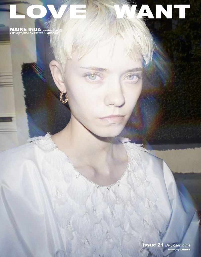 Close-up of a young fair-skinned woman with short blonde hair, wearing a white feather-detailed top and hoop earrings, in a fashion magazine.