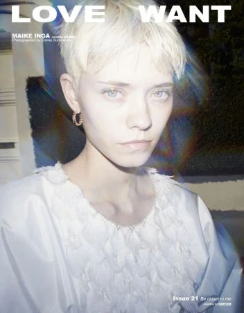 Close-up of a young fair-skinned woman with short blonde hair, wearing a white feather-detailed top and hoop earrings, in a fashion magazine.
