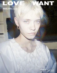 Close-up portrait of a blonde model wearing a textured white garment with prismatic light flares.
