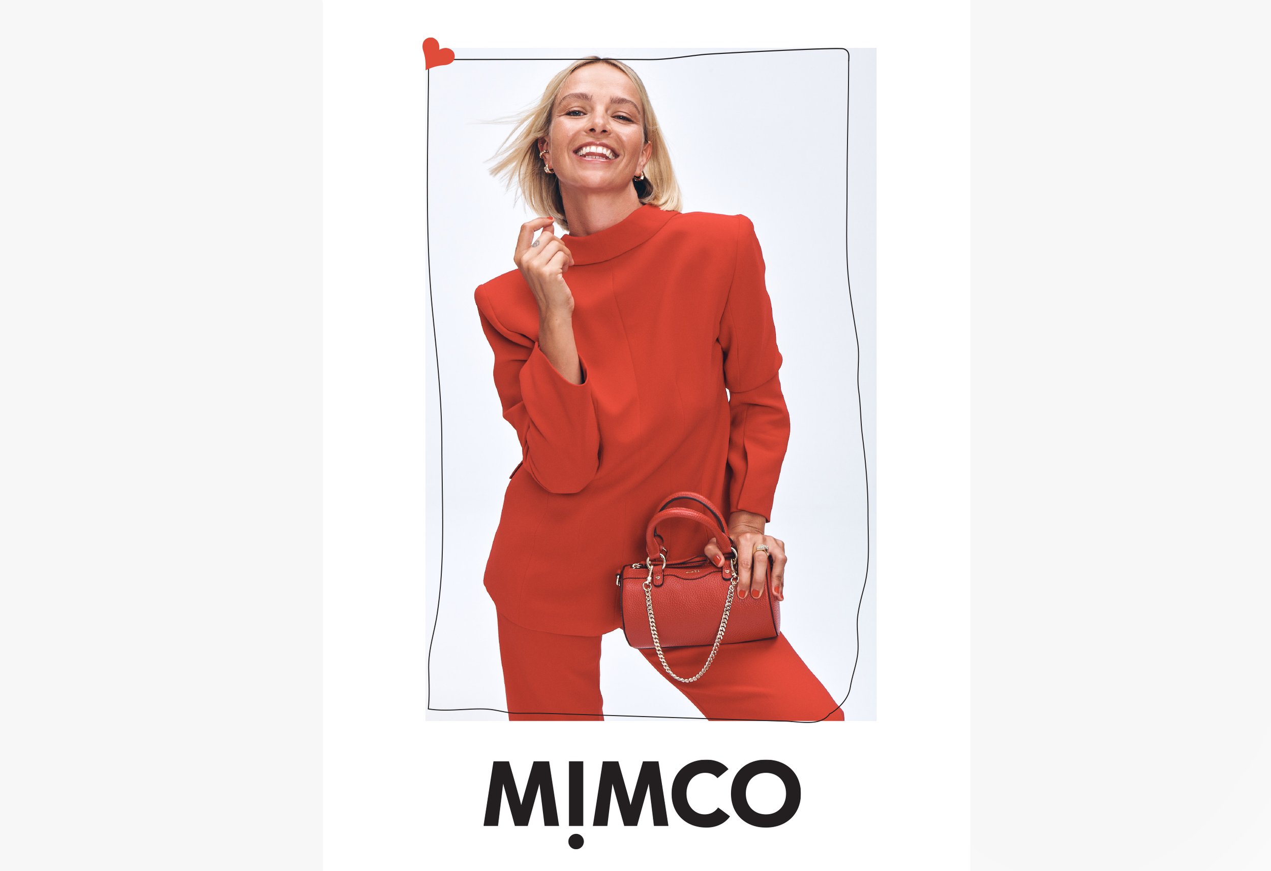 A blonde adult female smiles while posing in a red suit with a red handbag against a white background for a fashion-forward product shot.