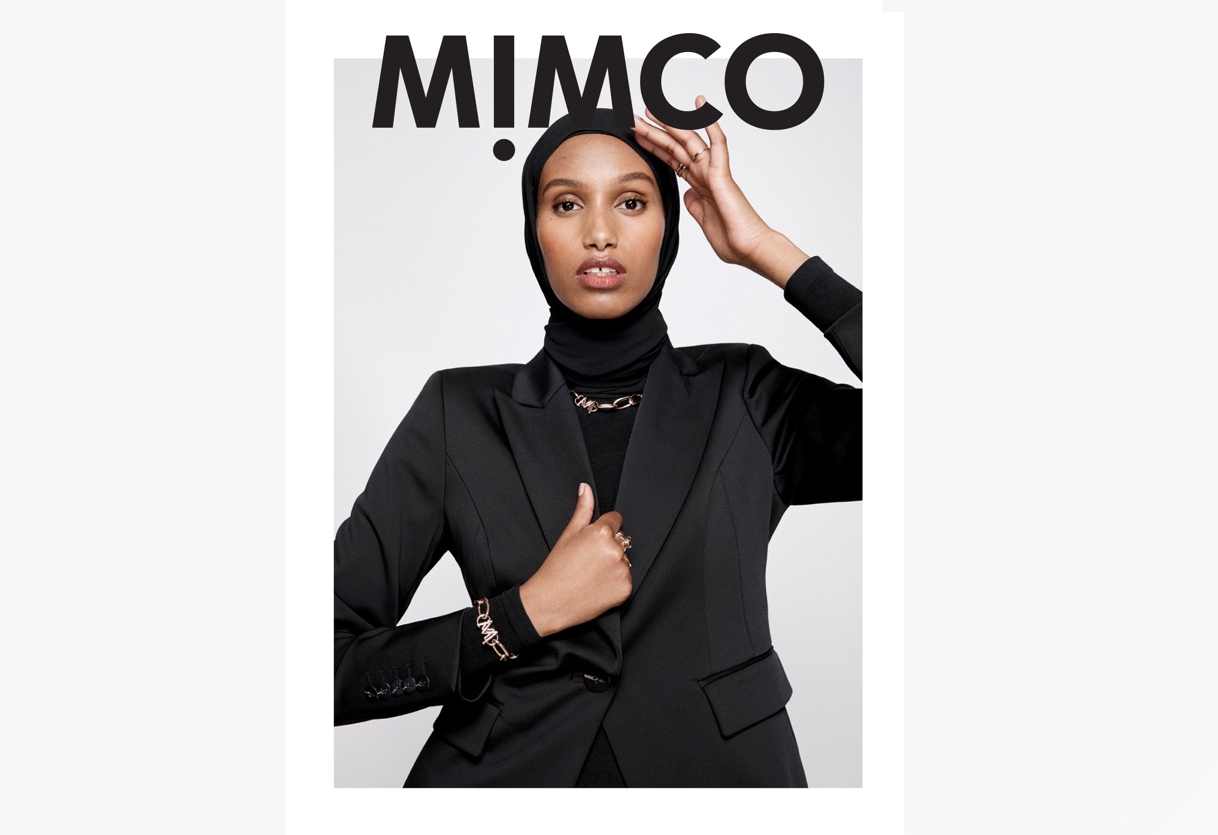 Fashion portrait of a woman wearing a black blazer and hijab, accessorized with gold jewelry against a white background with the MIMCO logo.
