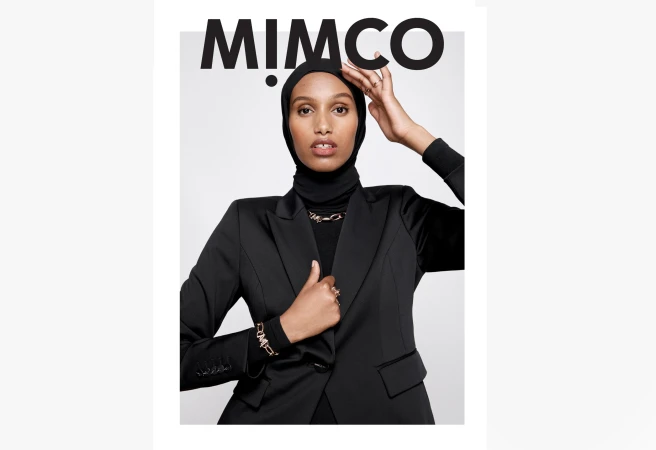 Fashion portrait of a woman wearing a black blazer and hijab, accessorized with gold jewelry against a white background with the MIMCO logo.