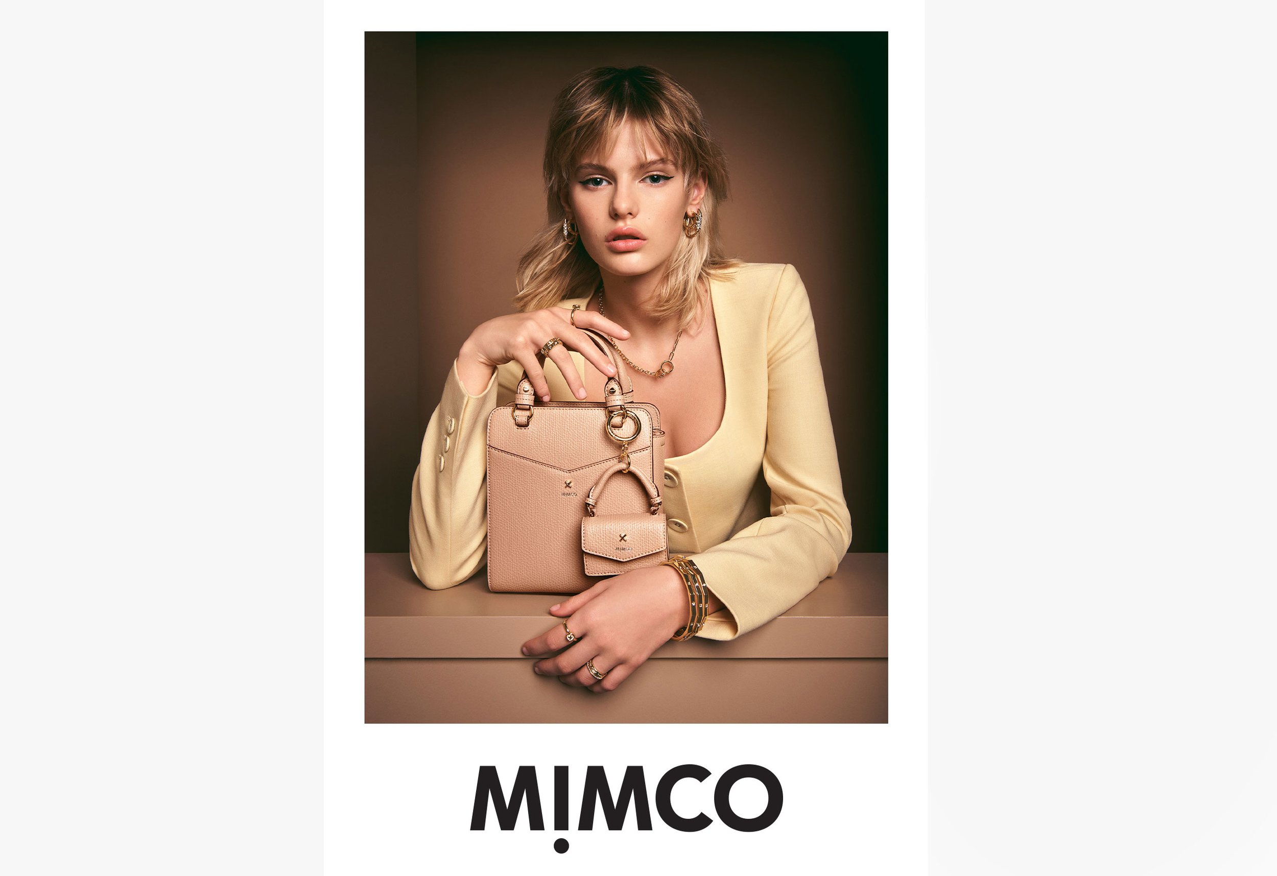 Fashion shot of a blonde woman in a blazer holding a purse with a matching coin purse against a neutral background. Accessories visible.